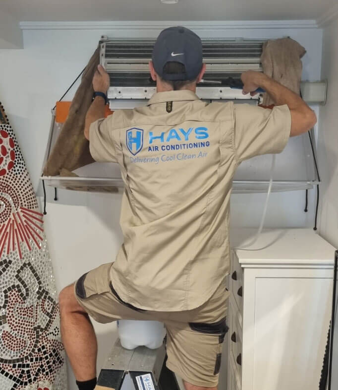 Hays Air Conditioning technician from Hays Air Conditioning using tools to deep clean an indoor air conditioning system for better efficiency and air quality.